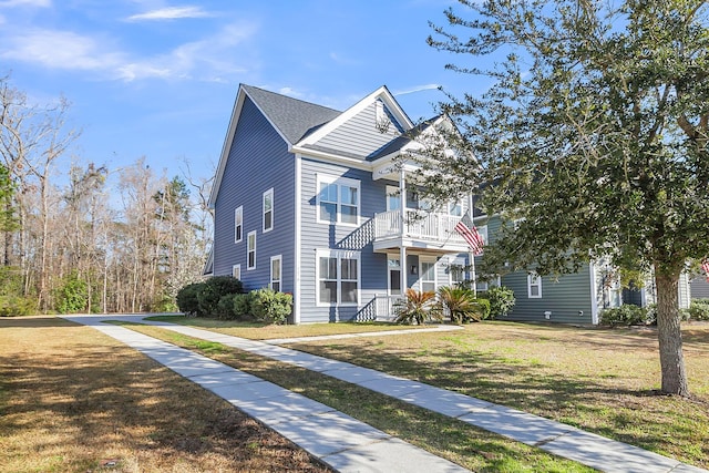 view of front of property with a front yard, a balcony, and roof with shingles