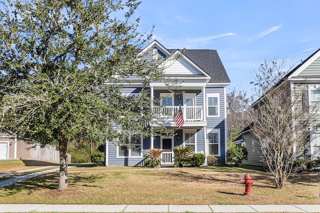 view of front facade with a balcony, a front lawn, and roof with shingles