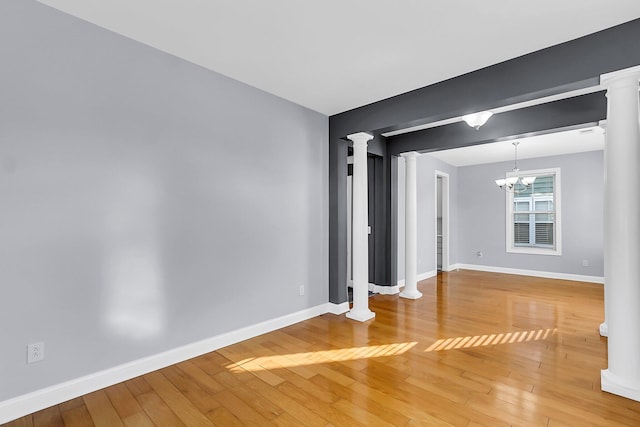 spare room with baseboards, light wood-style flooring, and ornate columns