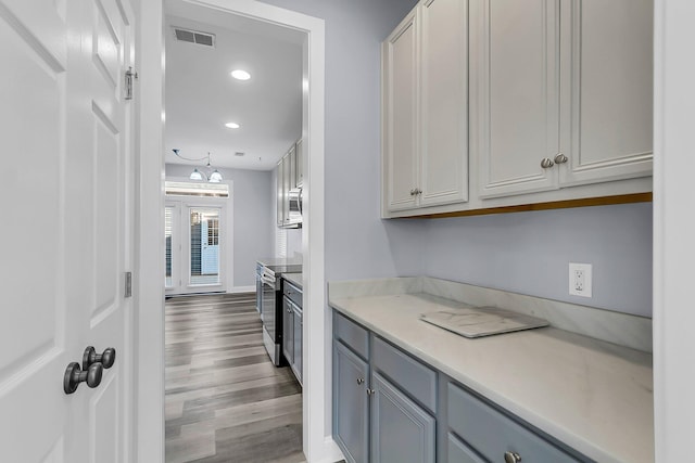 kitchen with wood finished floors, recessed lighting, gray cabinets, light countertops, and appliances with stainless steel finishes