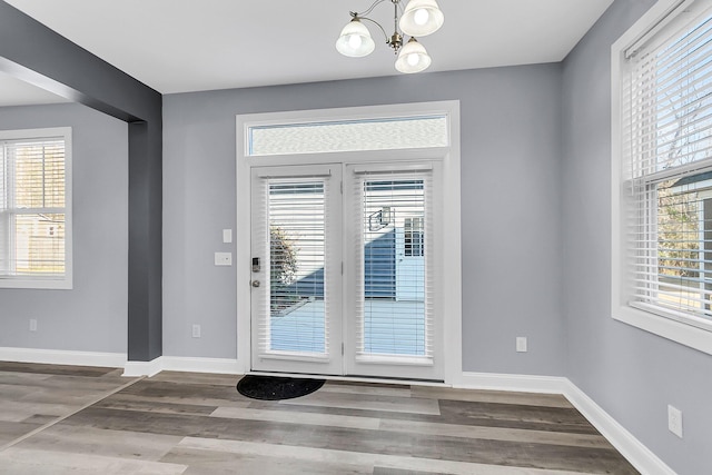 doorway to outside featuring an inviting chandelier, baseboards, and wood finished floors