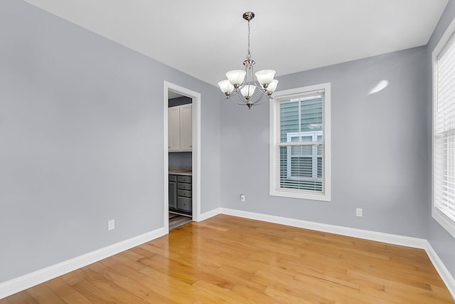 unfurnished room with light wood-style flooring, plenty of natural light, baseboards, and a chandelier