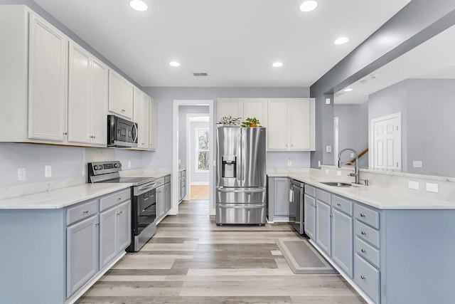 kitchen with light wood finished floors, visible vents, a peninsula, stainless steel appliances, and a sink