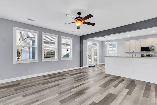 unfurnished living room with light wood finished floors, visible vents, a wealth of natural light, and a sink