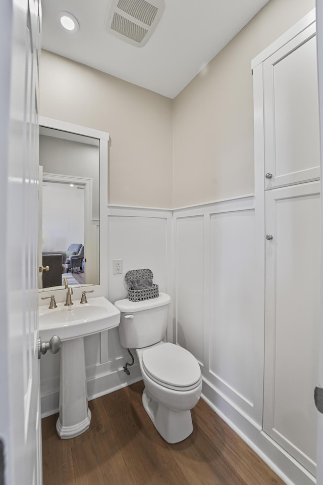 half bathroom with visible vents, wainscoting, toilet, and wood finished floors