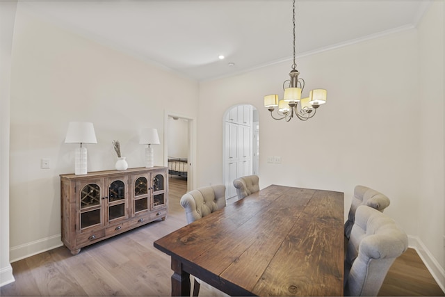 dining room featuring arched walkways, crown molding, baseboards, and wood finished floors