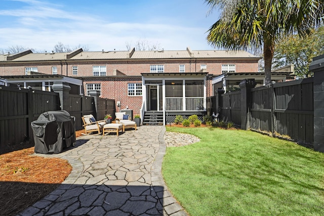 rear view of property with a fenced backyard, a sunroom, a lawn, a patio area, and brick siding