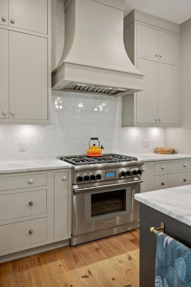 kitchen featuring backsplash, custom exhaust hood, light wood finished floors, and high end stove