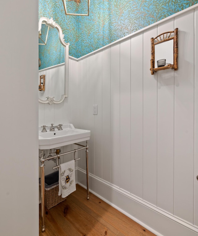 bathroom featuring a decorative wall, wallpapered walls, and wood finished floors