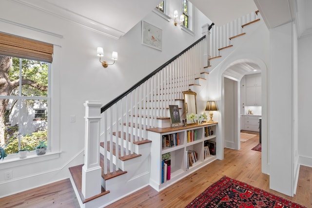 staircase with arched walkways, wood finished floors, and ornamental molding
