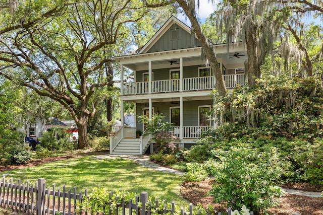 view of front of property featuring covered porch, board and batten siding, a ceiling fan, a front yard, and a balcony