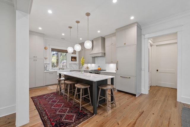 kitchen featuring a breakfast bar area, a center island, tasteful backsplash, light wood-style floors, and custom range hood