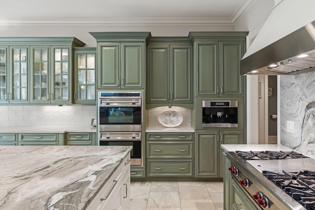 kitchen featuring wall chimney exhaust hood, light stone counters, ornamental molding, double oven, and decorative backsplash