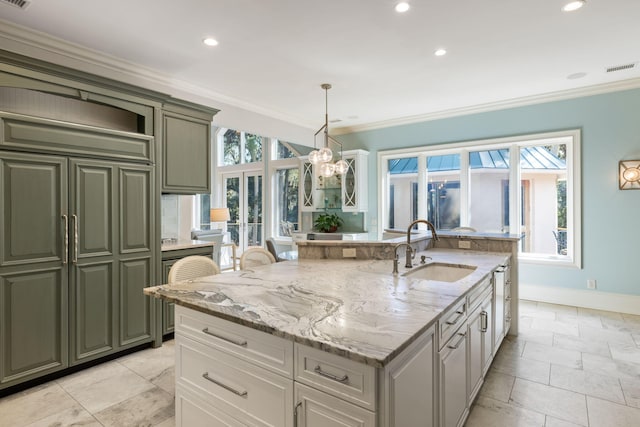 kitchen with sink, white cabinetry, crown molding, decorative light fixtures, and an island with sink