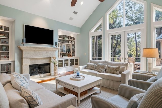 living room featuring french doors, built in features, hardwood / wood-style flooring, ceiling fan, and a fireplace