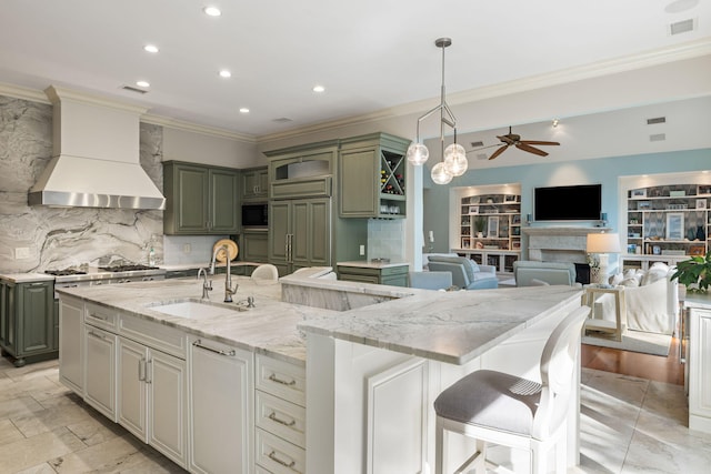 kitchen featuring sink, light stone countertops, green cabinetry, custom exhaust hood, and a large island with sink