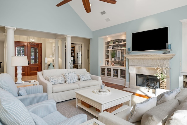 living room featuring built in features, decorative columns, a premium fireplace, and ceiling fan