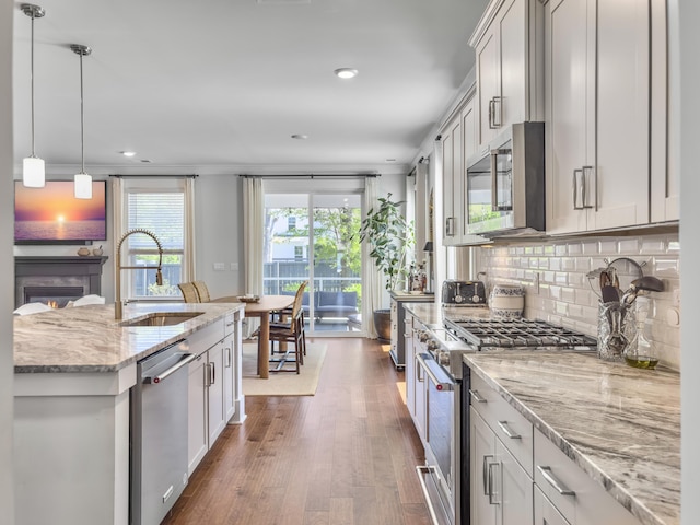 kitchen with a sink, light stone countertops, dark wood-type flooring, backsplash, and stainless steel appliances