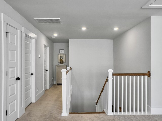 hall featuring visible vents, an upstairs landing, light colored carpet, and recessed lighting