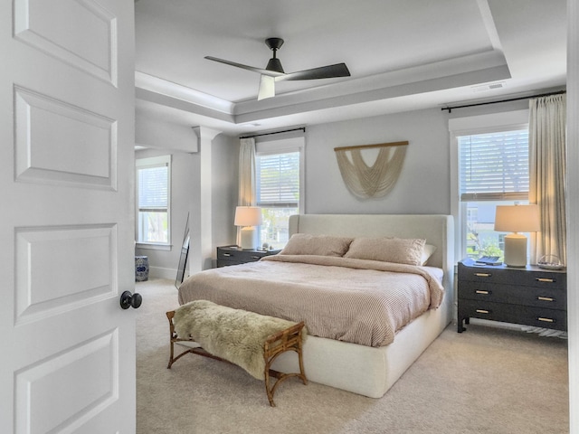bedroom with visible vents, baseboards, ceiling fan, a tray ceiling, and light colored carpet