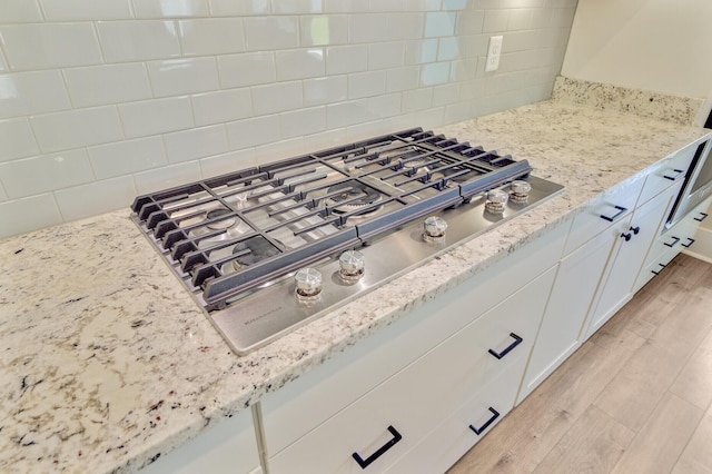 357 Parish Farms Dr, Summerville, SC 29486 - kitchen view of stainless steel gas stovetop, light stone countertops, white cabinets, backsplash, and light wood-type flooring