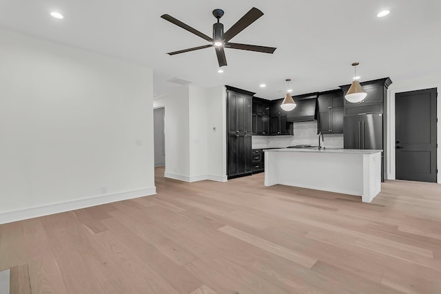 kitchen featuring tasteful backsplash, stainless steel fridge, an island with sink, and light hardwood / wood-style flooring