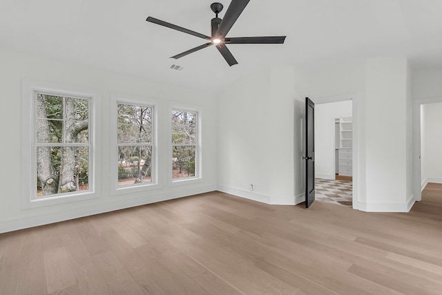 unfurnished bedroom featuring multiple windows, ceiling fan, a walk in closet, and light wood-type flooring