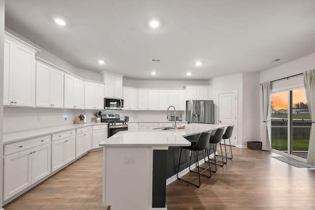 701 Squire Pope Rd, Summerville, SC 29486 - kitchen featuring stainless steel appliances, light wood finished floors, an island with sink, a kitchen bar, and white cabinetry