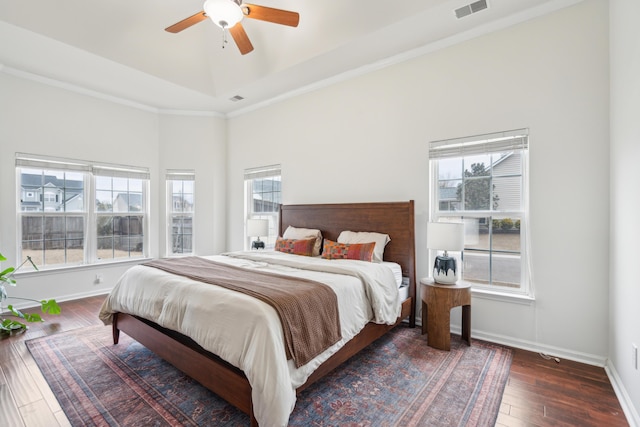 bedroom with dark wood-type flooring, ceiling fan, a tray ceiling, and multiple windows