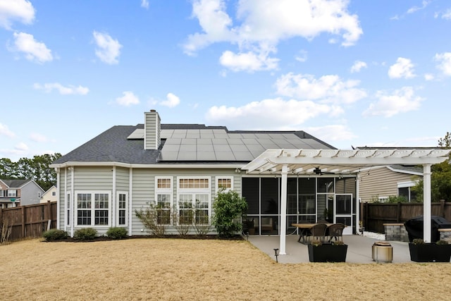 rear view of property with a pergola, a patio area, a sunroom, and solar panels