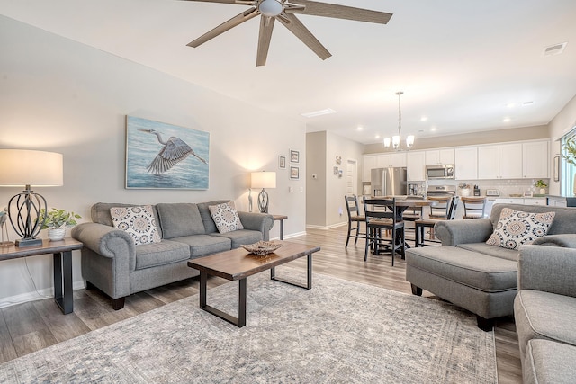 living area featuring visible vents, baseboards, light wood-style flooring, ceiling fan with notable chandelier, and recessed lighting