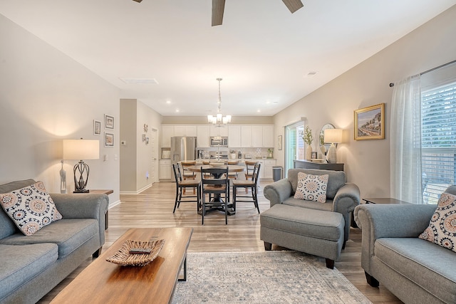 living room featuring light wood finished floors, plenty of natural light, baseboards, and ceiling fan with notable chandelier