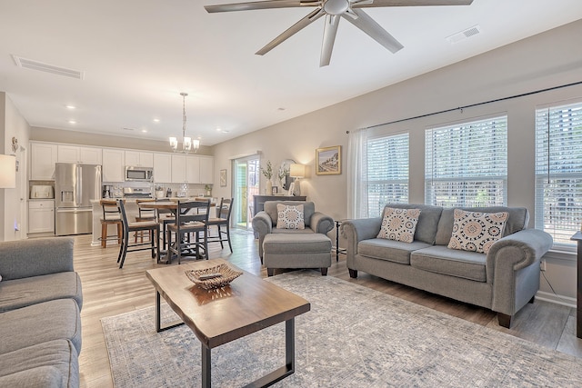 living area featuring recessed lighting, light wood-style flooring, visible vents, and ceiling fan with notable chandelier