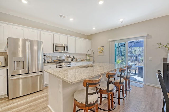 kitchen featuring stainless steel appliances, decorative backsplash, a sink, light wood-type flooring, and a kitchen bar