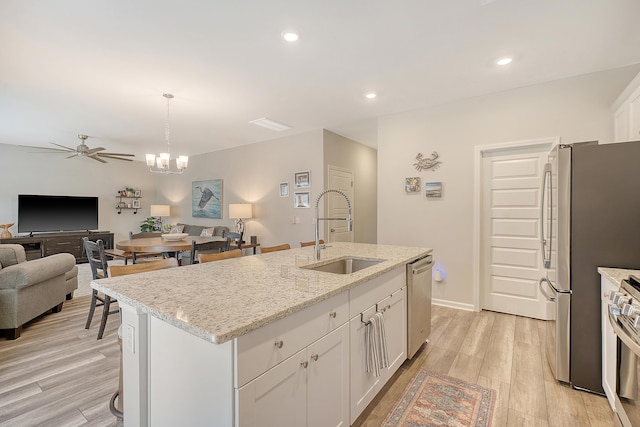 kitchen featuring appliances with stainless steel finishes, open floor plan, white cabinetry, a sink, and light wood-type flooring