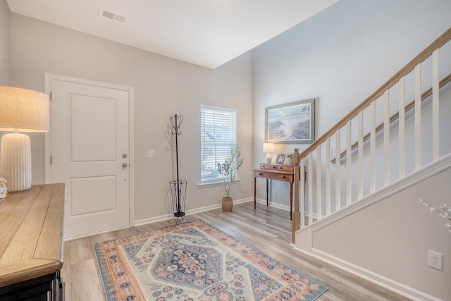 foyer entrance featuring baseboards, stairs, visible vents, and wood finished floors