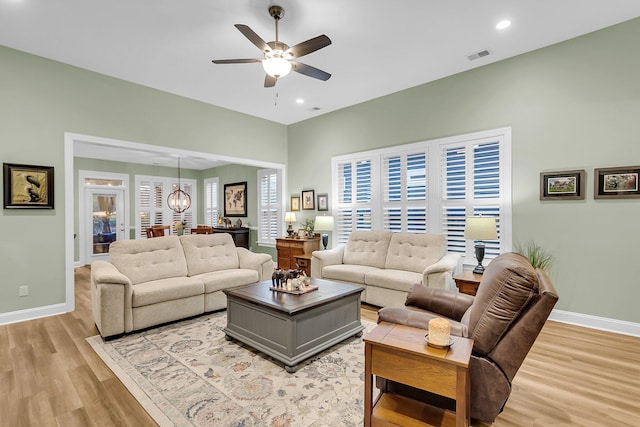 living room with light wood-type flooring, visible vents, ceiling fan with notable chandelier, recessed lighting, and baseboards