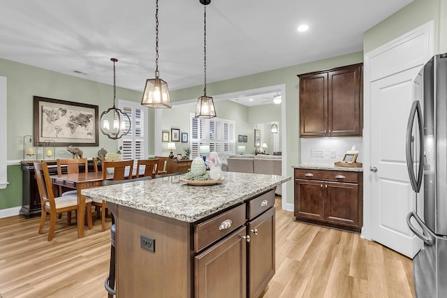 kitchen with light stone counters, a kitchen island, freestanding refrigerator, and light wood-style floors