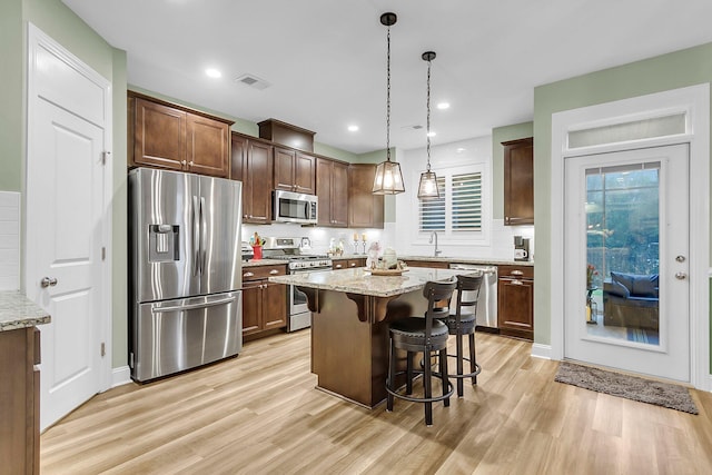 kitchen featuring visible vents, light wood-type flooring, a kitchen bar, light stone counters, and appliances with stainless steel finishes