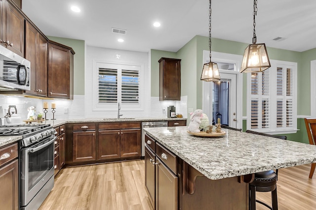 kitchen featuring light stone countertops, visible vents, light wood finished floors, a sink, and appliances with stainless steel finishes