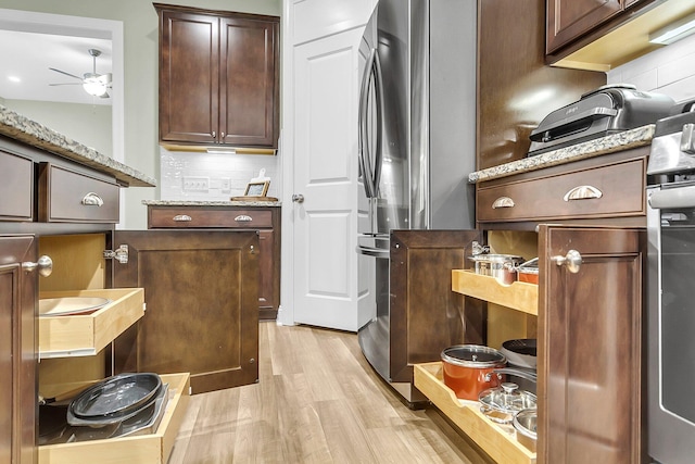 kitchen with a ceiling fan, light stone countertops, dark brown cabinetry, light wood-style floors, and tasteful backsplash