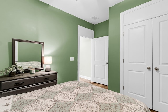 bedroom with wood finished floors, visible vents, and a closet