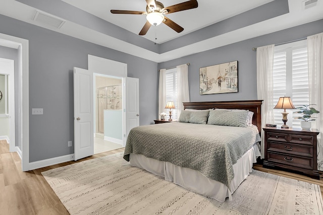 bedroom featuring a tray ceiling, visible vents, baseboards, and light wood finished floors