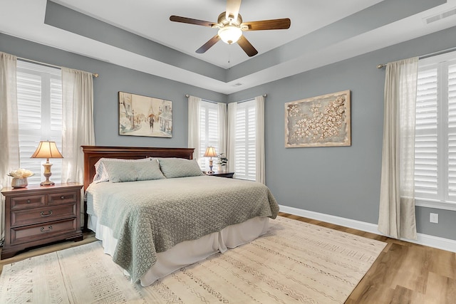 bedroom with visible vents, a ceiling fan, a tray ceiling, wood finished floors, and baseboards