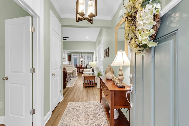 corridor featuring an inviting chandelier, crown molding, and light wood finished floors