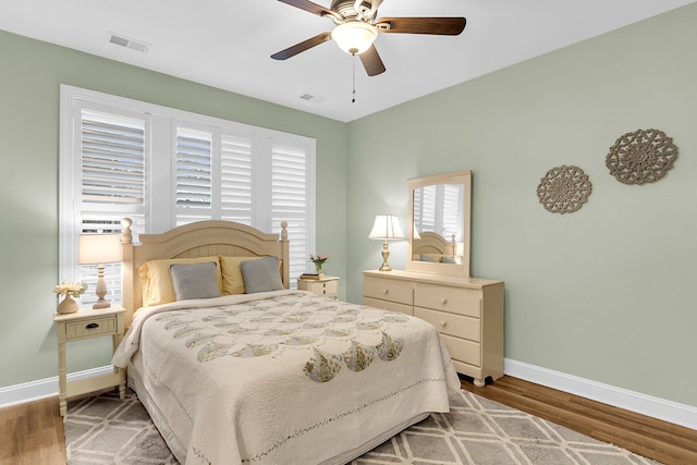 bedroom with a ceiling fan, visible vents, wood finished floors, and baseboards