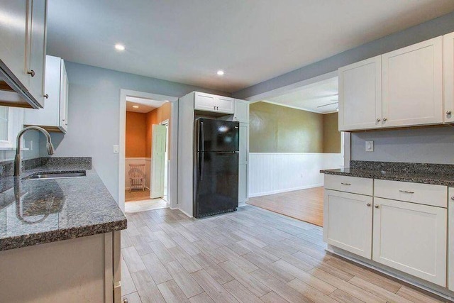 kitchen with a sink, white cabinets, wainscoting, freestanding refrigerator, and dark stone counters