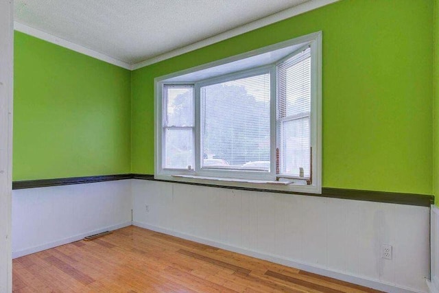 unfurnished room featuring light wood finished floors, visible vents, a textured ceiling, and wainscoting