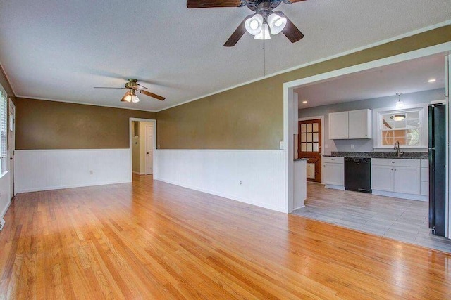 unfurnished living room featuring light wood-style floors, a wainscoted wall, a sink, and a textured ceiling