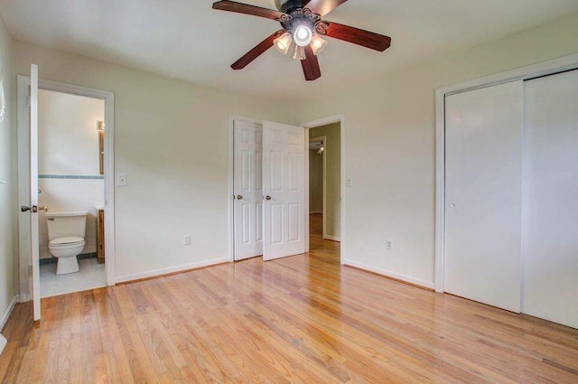 unfurnished bedroom featuring light wood-style floors, ensuite bath, a ceiling fan, and tile walls